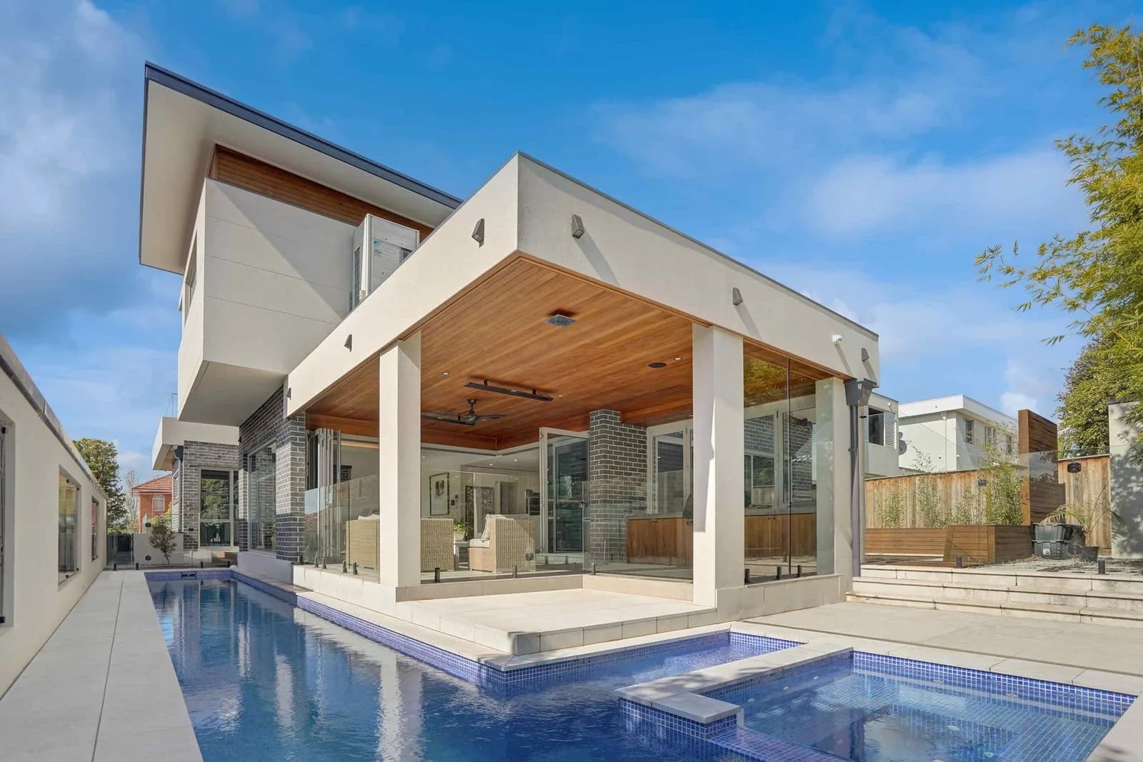 Rear exterior showcasing the covered alfresco area, timber-look soffit, glass pool fencing, pool, spa and landscaped outdoor entertaining space