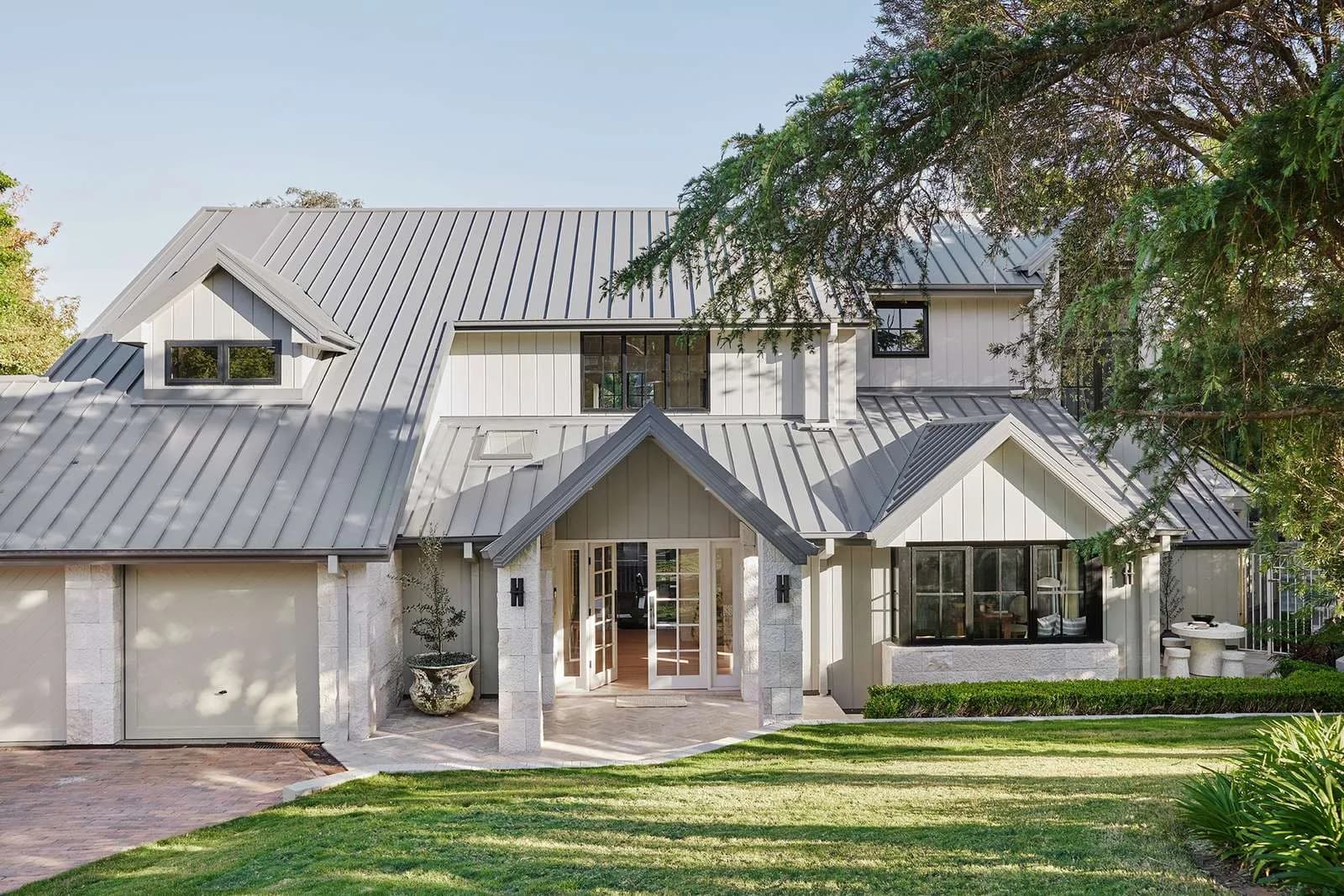 Transformed Urban Farmhouse façade with light cladding, standing seam roof, gabled entry, refreshed brickwork and landscaped front garden